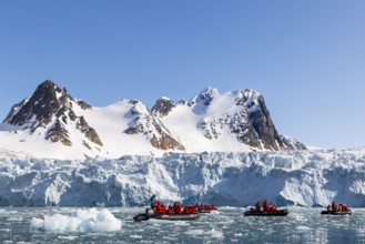 Group of Zodiacs in front of glacier and mountain range with snow, sea, Fugelfjorden, Spitsbergen,