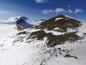 Near a snow-covered hilltop with rocks on the descent under a clear sky, aerial view, Aragaz,