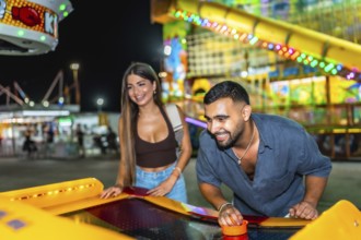 Young man and woman having fun playing air hockey at amusement park at night, enjoying their