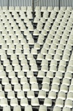Rows of empty white seats fill a large stadium, creating a uniform pattern. The seating arrangement