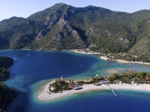 Panoramic picture with coastline and sandbank, surrounded by turquoise water and green hills,
