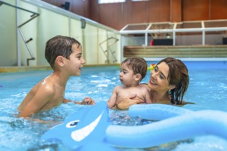 Mother and children enjoying time together, playing with inflatable toys in a swimming pool,