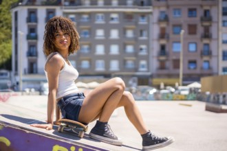 Young woman sitting on her skateboard atop a ramp in an urban skatepark, soaking up the sun on a
