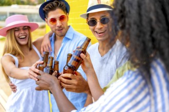 Cheerful multi ethnic friends enjoying a summer party, toasting with beer bottles against a vibrant