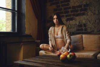 A pregnant woman sits on the couch and pours water into a glass