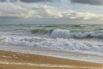 Powerful ocean waves wash over a sandy beach, creating white foam against a backdrop of dramatic