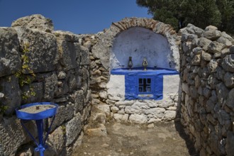Stone chapel with blue window amidst ancient ruins, surrounded by natural walls and a deep blue