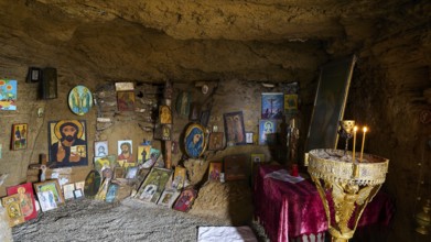 Religious sanctuary in a cave with orthodox icons and burning candles on an altar, chapel, Agios