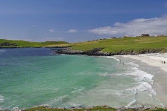 A picturesque beach with turquoise waters and gentle waves under a blue sky, surrounded by green