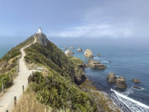 Nugget Point Lighthouse with Nugget Rocks in front of a blue sky, South Island, New Zealand,