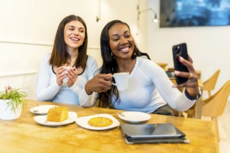 Two happy female friends are taking a selfie with smartphone while enjoying coffee and cake in a