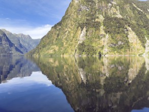 Mountains with reflections in the water against a blue sky in Doubtful Sound, South Island, New