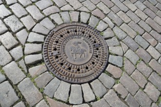 Round manhole cover with city coat of arms and inscription, state capital, paving stones, floor,