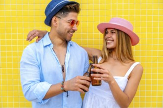 Young stylish tourists toasting with beer bottles, enjoying summer vacation together against a