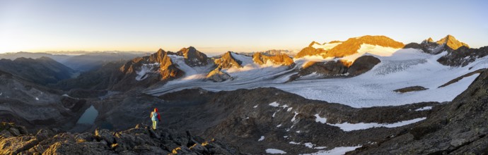 Mountaineer in front of picturesque high mountain landscape at sunrise with alpenglow, blue glacial
