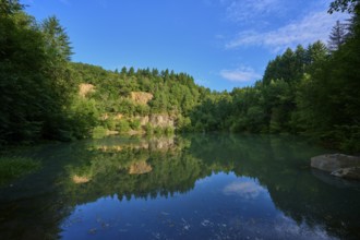 Tranquil lake in the middle of a forest with a clear water surface that reflects the sky,