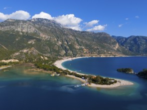 View of a beach with a peninsula surrounded by mountains and blue sea under a clear sky with