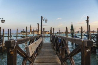 Wooden pier with gondolas and lamps leading to san giorgio maggiore in venice at sunset, creating a