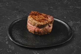 Perfectly seared filet mignon sits on a dark plate, highlighting its rich color and inviting look.