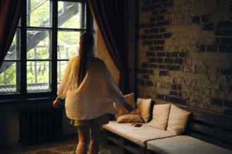 Rear view of a woman walking across the room to the sofa. The setting features exposed brick walls,