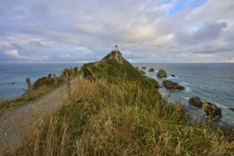 Path leading to a lighthouse on a cliff overlooking the sea under a cloudy sky, summer, Nugget