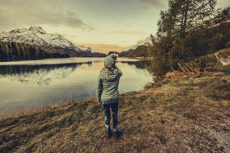 Woman by the lake in autumn Engadine in Switzerland with snow-covered mountain peaks