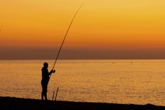 A man fishing just in front of sunrise on the Costa Rei, a coastline of the Italian island of