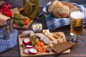 Rustic snack with sausage, cheese, beer, mustard, radishes and bread on a laid table