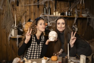 Two friends pose playfully in a decorated room for Halloween, surrounded by candles, pumpkins, and