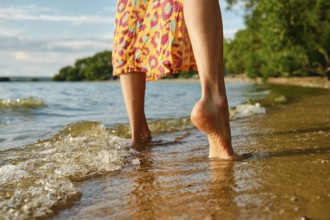 Low angle rear view of bare female feet on a calm beach. The gentle waves lap female feet
