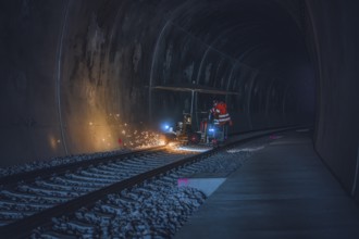 A worker in an orange waistcoat works on the rails in a dark tunnel while sparks fly, grinding work