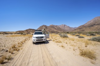 Young man standing in the open door of an off-road vehicle, sandy track, desert landscape with