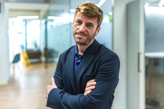 Portrait of a smiling businessman standing with crossed arms in a modern office, exuding confidence
