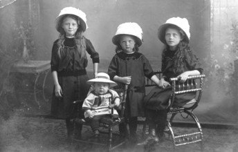 Three young girls with child, 1920s, Four girls wearing hats and dark clothes, standing and sitting