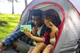 Two young campers are taking a selfie inside their tent, enjoying a moment of fun during their