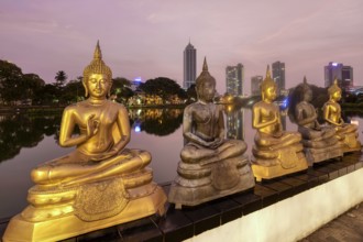 Buddha statues of Seema Malaka Temple at Beira Lake at sunset, Colombo skyline behind, Sri Lanka