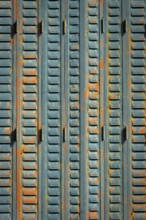 A close-up view of weathered metal shutters displaying a mix of blue paint and rust. The surface