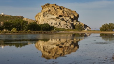 Large rock formation calmly reflected on the surface of the water, surrounded by nature, Kalikatsou