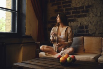 In a cozy home setting, a pregnant woman sits comfortably on a couch with a glass of mineral water,