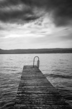 A rustic jetty stretches into the calm waters of Lake Geneva, framed by gentle waves and majestic