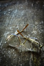 Unique vintage eyeglasses with a simple design rest on a weathered wooden surface, basking in warm