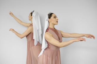 Two ballerinas standing back to back and waving hands on grey background
