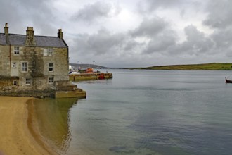 A stone cottage stands on the sandy shore of a calm loch under a cloudy sky, Lerwick, crime series,