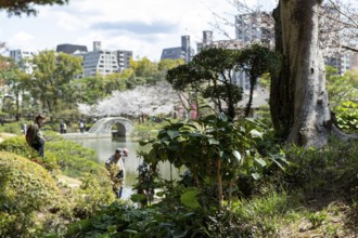 Tourists in the Shukkei-en with green plants, trees and Takuei-chi pond in spring, historical