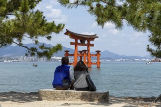 A couple on the beach looking at the torii in the water, landmark, tourist attraction, UNESCO World