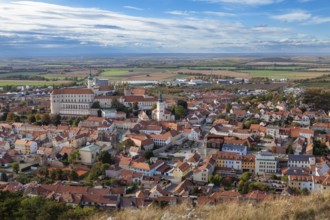 Panoramic view of a town with a historic castle and churches, surrounded by fields and clouds,