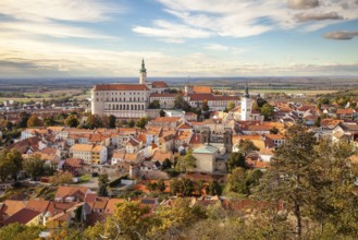 Panorama of a historic town with castle and churches, surrounded by autumn trees and a wide sky,