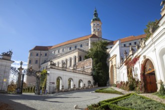 A magnificent castle with a richly decorated entrance gate, surrounded by trees under a blue sky,