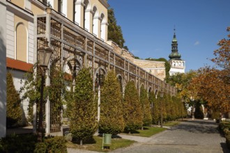A well-tended garden with trees and antique lanterns in front of a series of arches, Mikulov