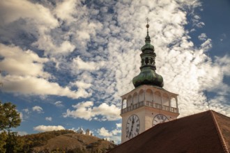 A church tower with a clock sits enthroned against a cloudy sky and overlooks a hill, Mikulov